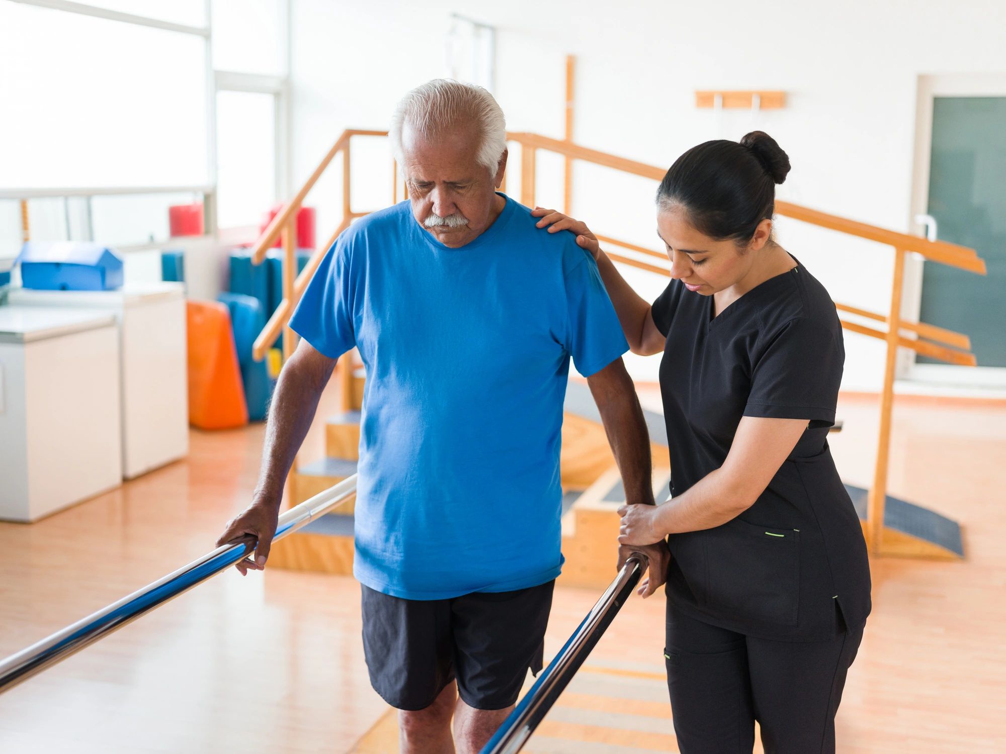 Therapy session helping a senior patient walk with support bars